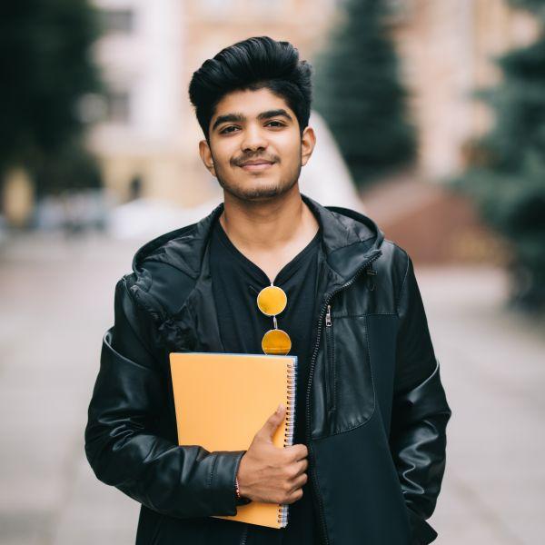 Home 24 handsome young indian student man holding notebooks while standing street